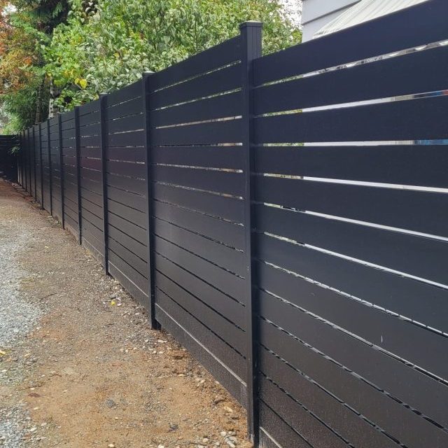 Black aluminum privacy fence with horizontal slats and gap spacing installed along a residential property.
